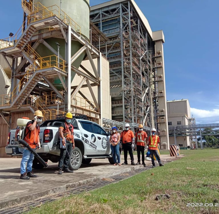 Industrial workers in safety gear standing by a pickup truck outside a power plant facility.