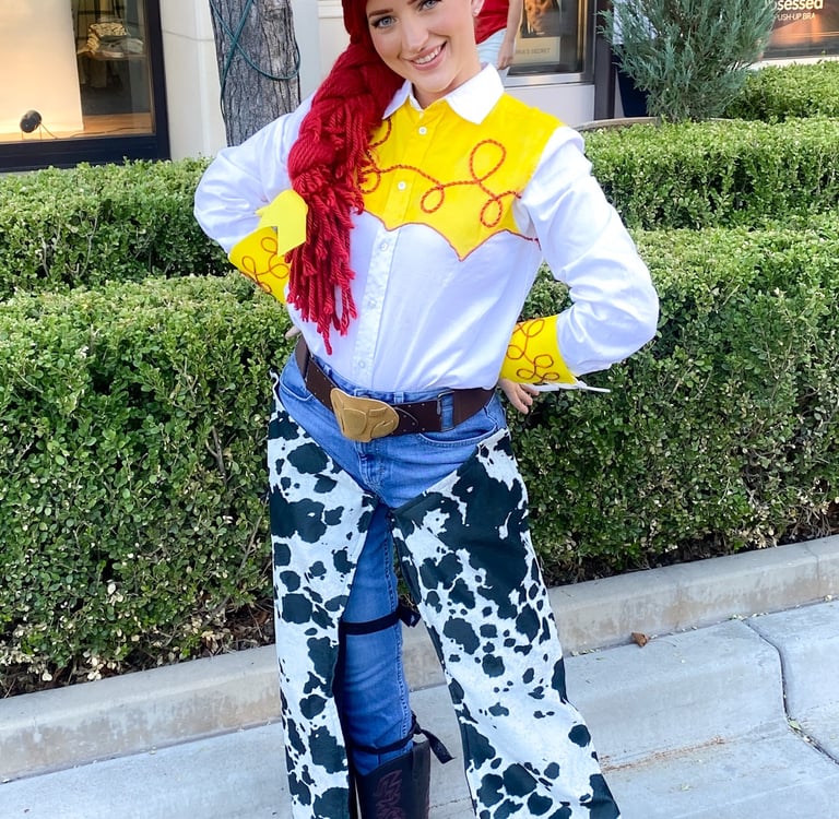 A smiling woman wearing a Jessie from Toy Story costume with a cow print outfit and red cowgirl hat.