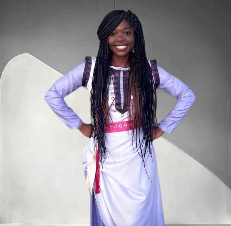 Smiling woman with long box braids wearing a light purple traditional African dress.