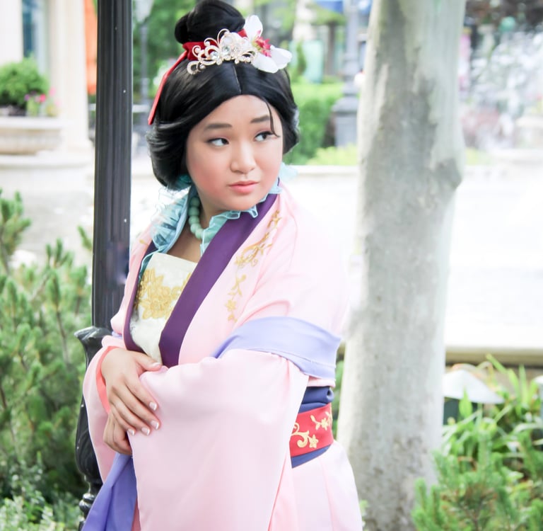 A young woman in a pink and purple Mulan cosplay outfit with traditional Chinese hair accessories.