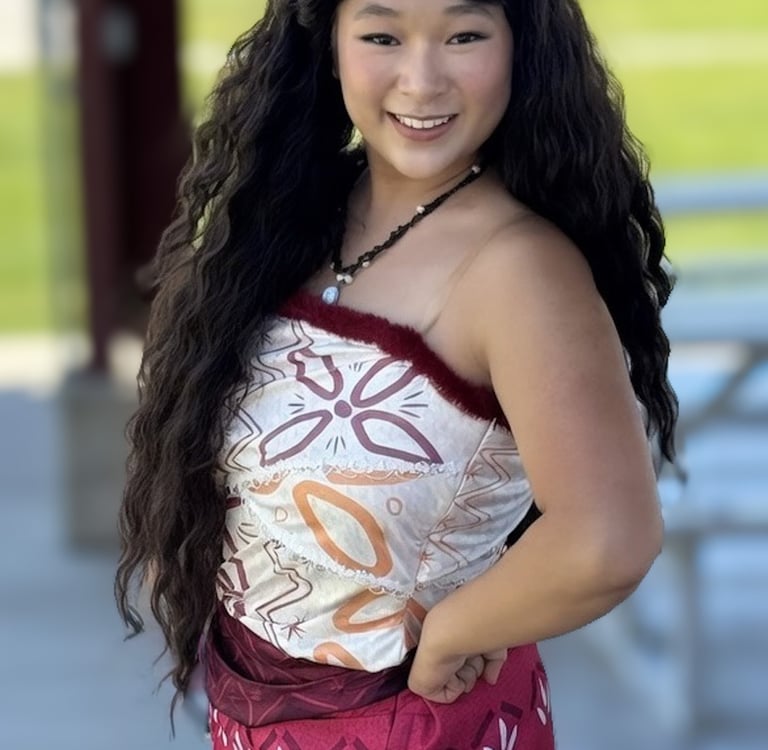 A girl in a Moana costume with long curly hair and a patterned Polynesian dress.