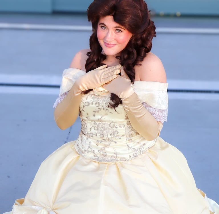 A woman in a Belle cosplay costume with a yellow ballroom gown and long gold gloves.