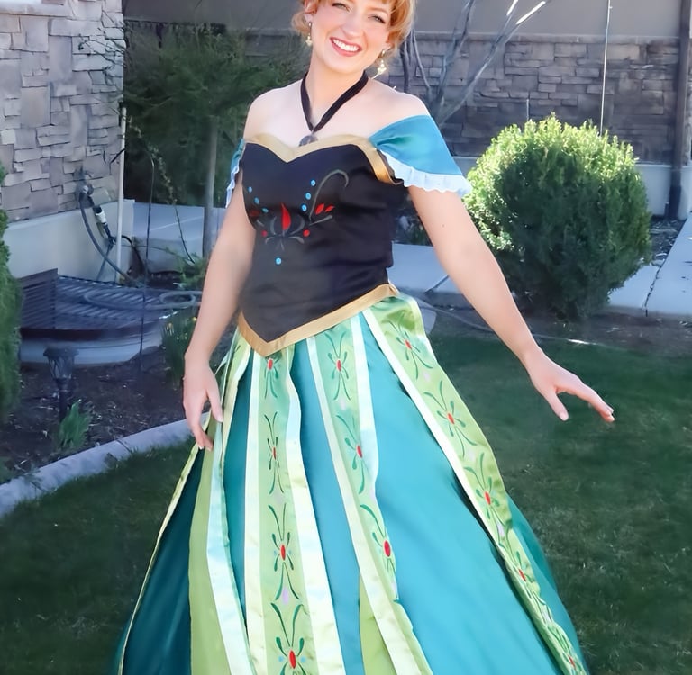 Smiling woman in a detailed Princess Anna coronation dress cosplay standing in a garden.