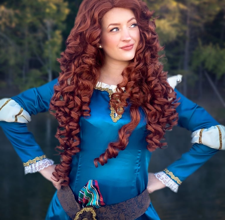 A woman in a Merida cosplay featuring long curly red hair and a teal medieval gown outdoors.