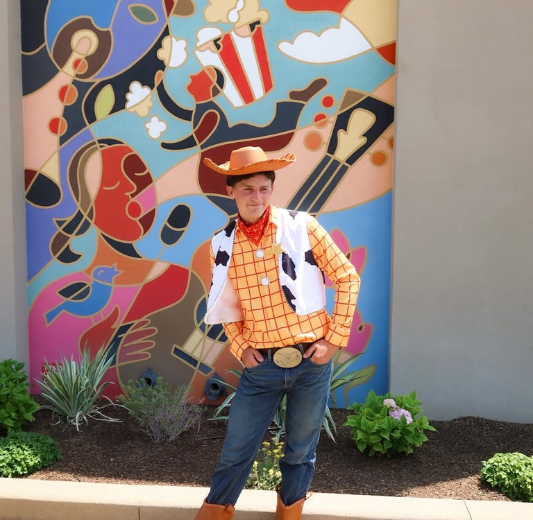 A man wearing a Woody from Toy Story cowboy costume posing in front of a colorful abstract mural.