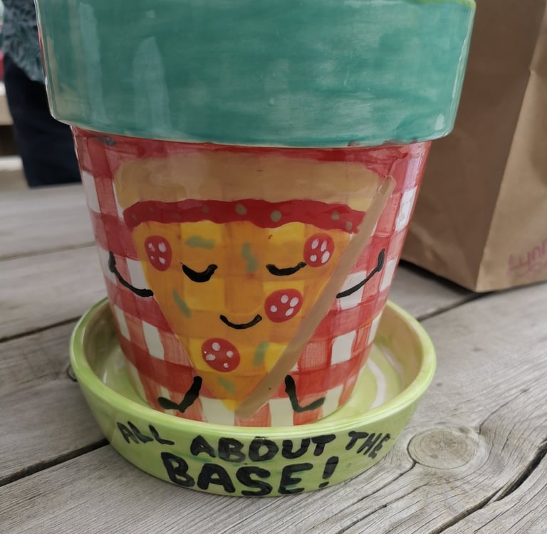 Hand-painted ceramic pizza planter on a wooden table with a smiling pizza slice design.