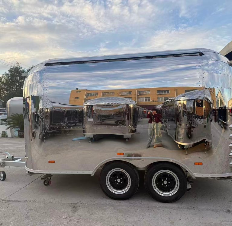Polished chrome airstream food trailer parked outdoors with a highly reflective mirror finish.