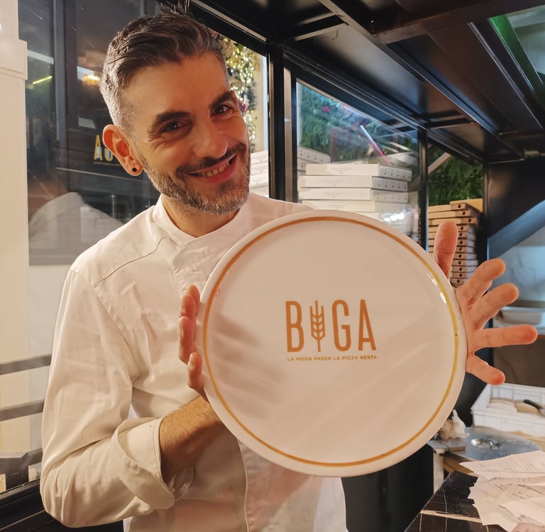 Simone Nicolosi, pizzaiolo di BIGA Milano, mostra un piatto con il logo della pizzeria all’interno del locale