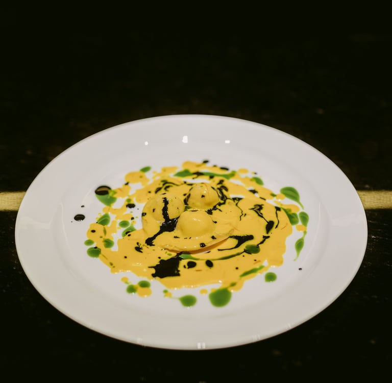 Raviolo signature dello chef Riccardo Quadri con salsa gialla e decorazioni verdi e nere.
