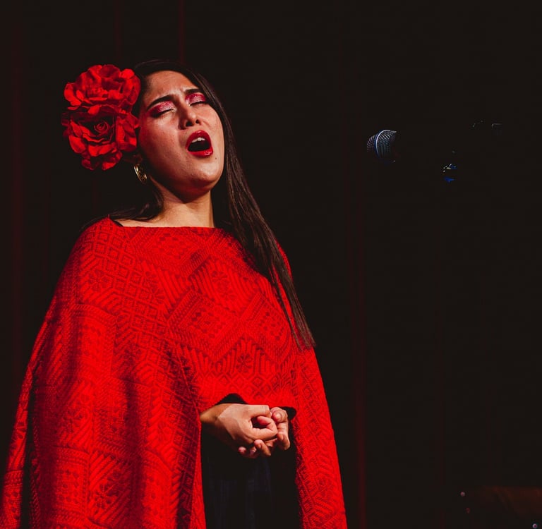 Female singer performing in a red embroidered poncho with a flower in her hair at a live concert.
