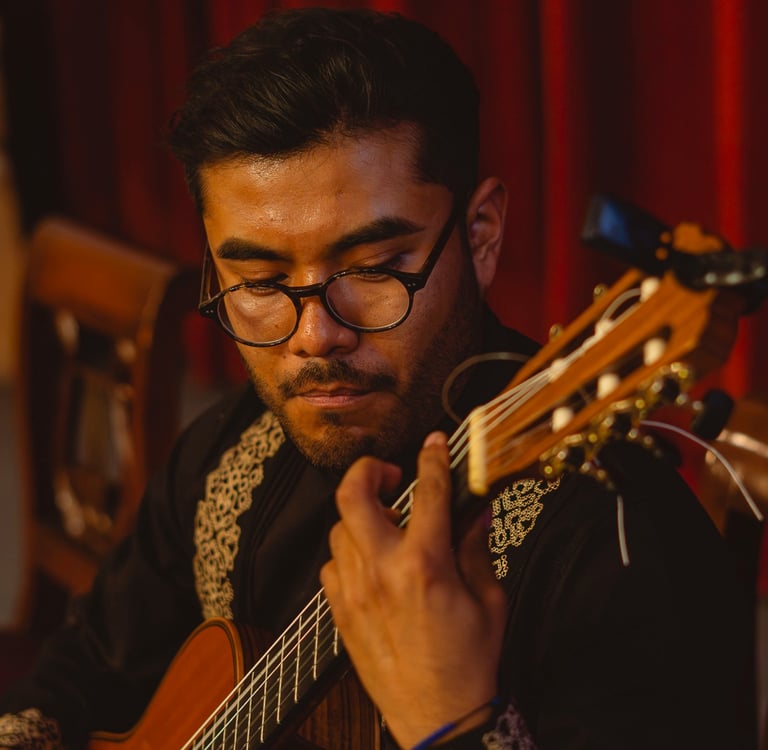 A musician wearing glasses plays a classical acoustic guitar during a live performance.