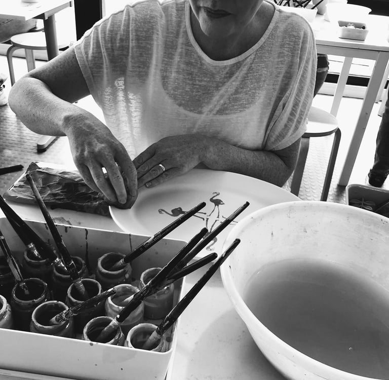 Patricia Madden Artist paints a ceramic plate with flamingo designs in a pottery studio workshop.