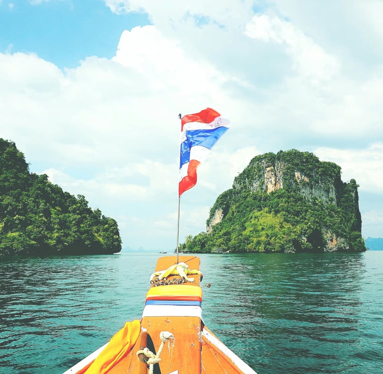A traditional Thai longtail boat sailing past limestone islands in the tropical waters of Thailand.