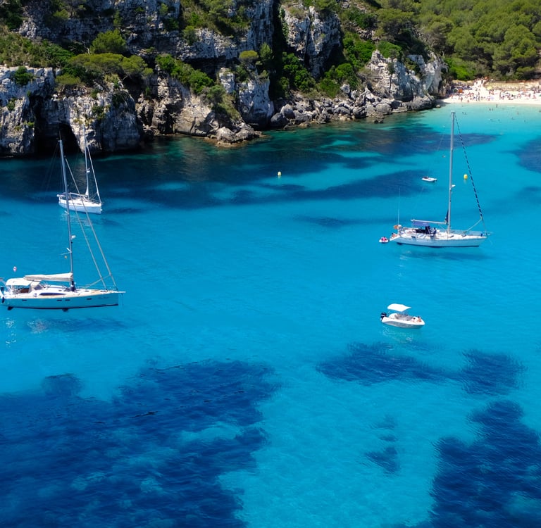 Aerial view of sailboats in the crystal clear turquoise water of Cala Macarella beach in Menorca.