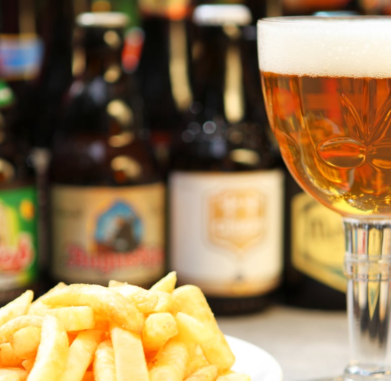 A glass of Belgian craft beer served with golden french fries and bottled beers in the background.