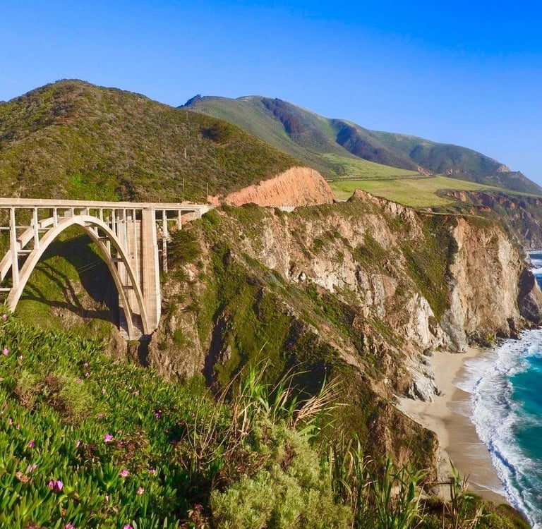 Bixby Creek Bridge on the Big Sur coast of California with ocean waves and green cliffs.