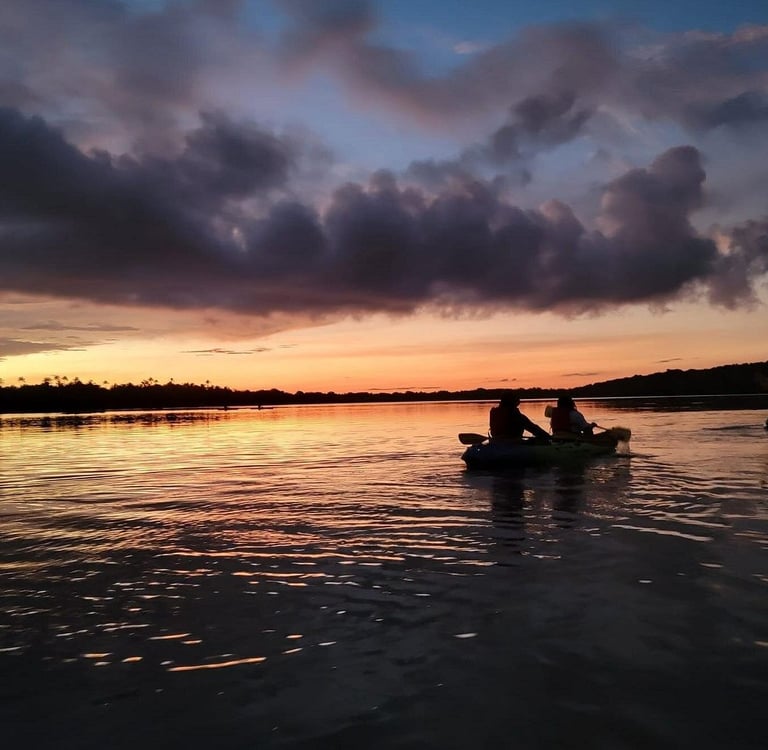 Two people in a kayak enjoy a calm sunset paddle on a wide river with golden reflections.