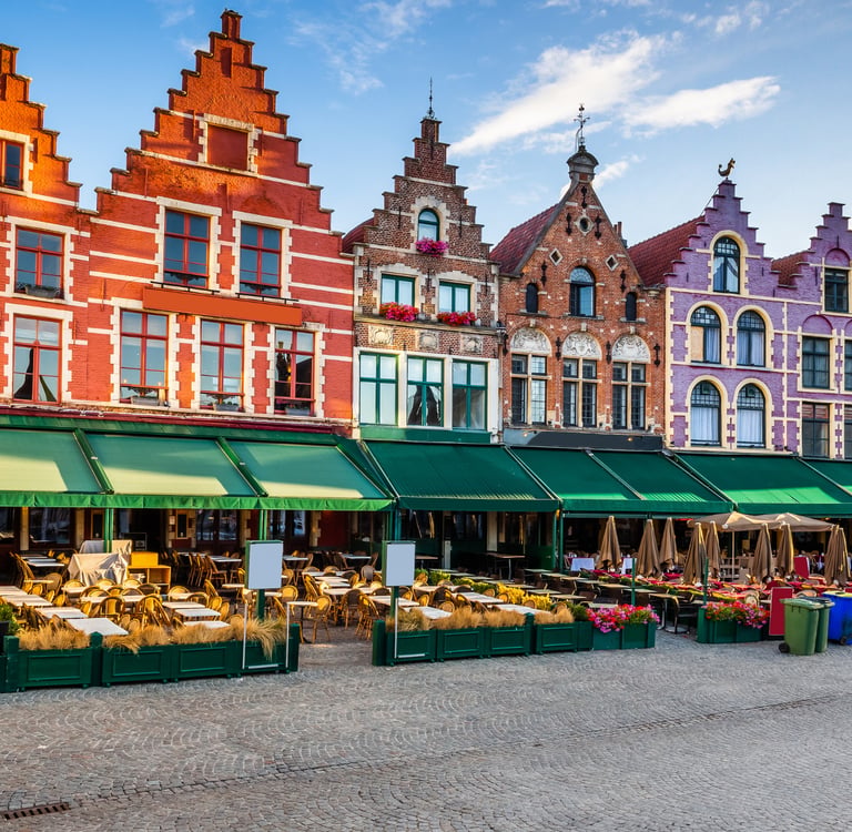 Colorful medieval guildhalls and outdoor cafes at the Market Square in Bruges, Belgium.