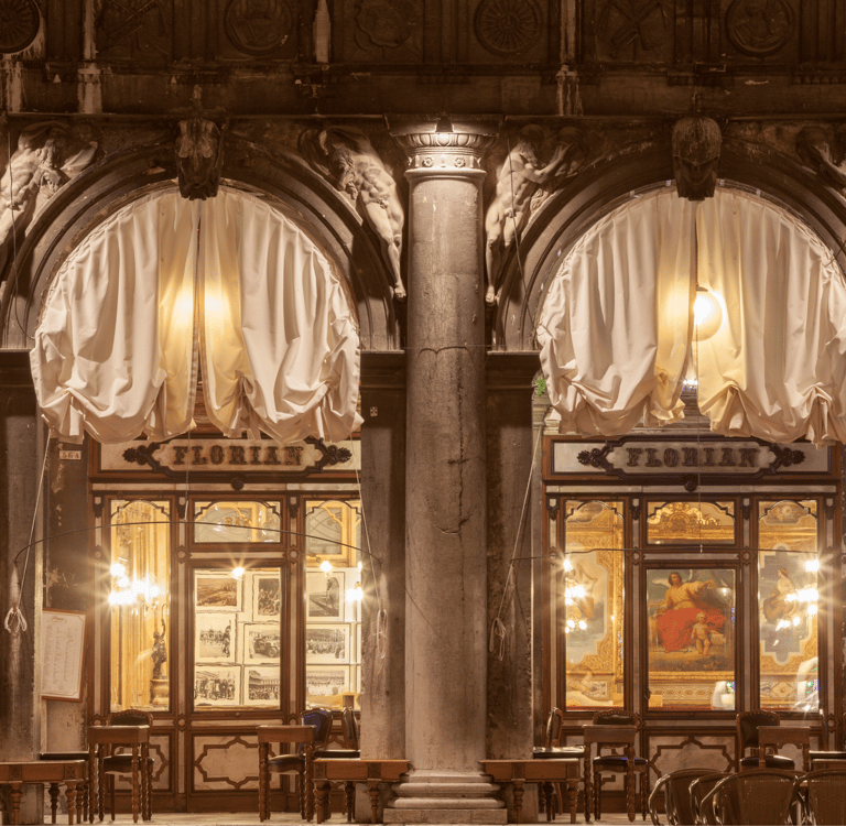 Exterior view of the historic Caffe Florian in St. Mark's Square, Venice, featuring arched windows and ornate stone columns.