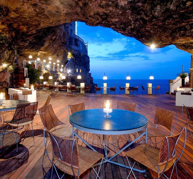 Luxury fine dining restaurant inside a coastal sea cave overlooking the blue ocean at twilight.