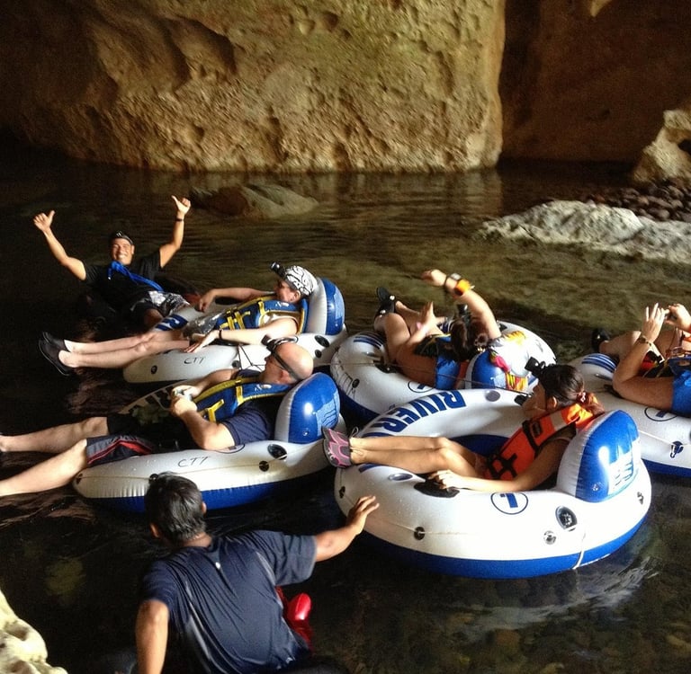 A group of tourists wearing life jackets and cave tubing in an underground river cave in Belize.