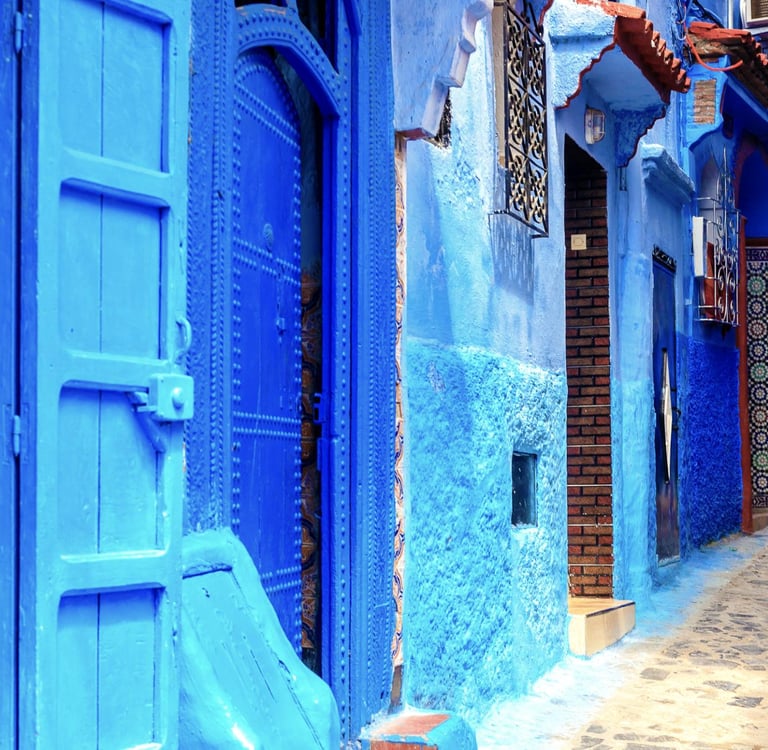 A narrow cobblestone street in Chefchaouen, Morocco, featuring traditional blue painted walls and doors.