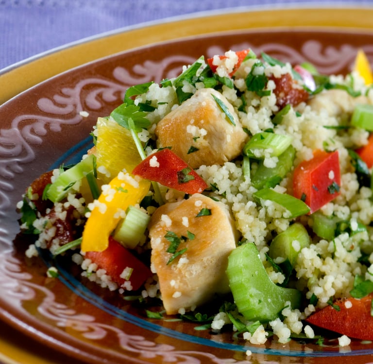 A healthy chicken couscous salad with bell peppers and celery on a brown ceramic plate.