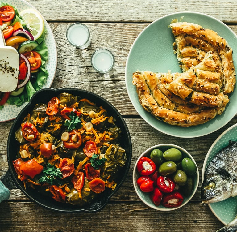 Traditional Greek food spread with grilled fish, feta salad, spanakopita, and olives on a rustic wooden table.