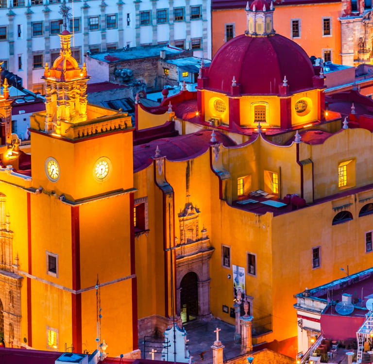 Illuminated yellow facade and red dome of Basilica of Our Lady of Guanajuato at twilight in Mexico.