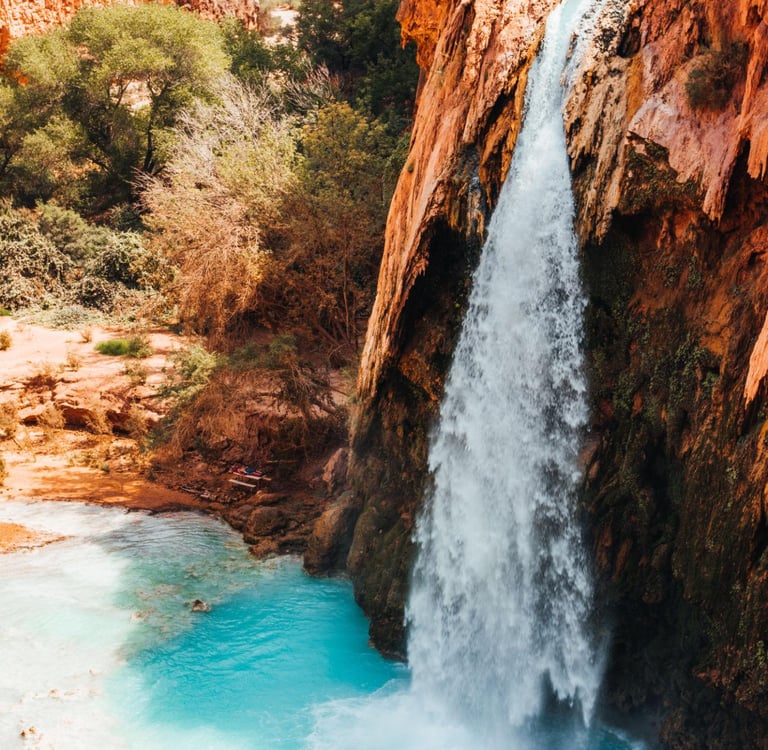A high-angle view of Havasu Falls cascading into a bright turquoise pool within the Grand Canyon.