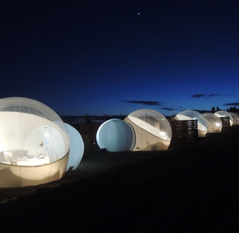 Illuminated luxury bubble hotel tents for glamping under a dark starry night sky.