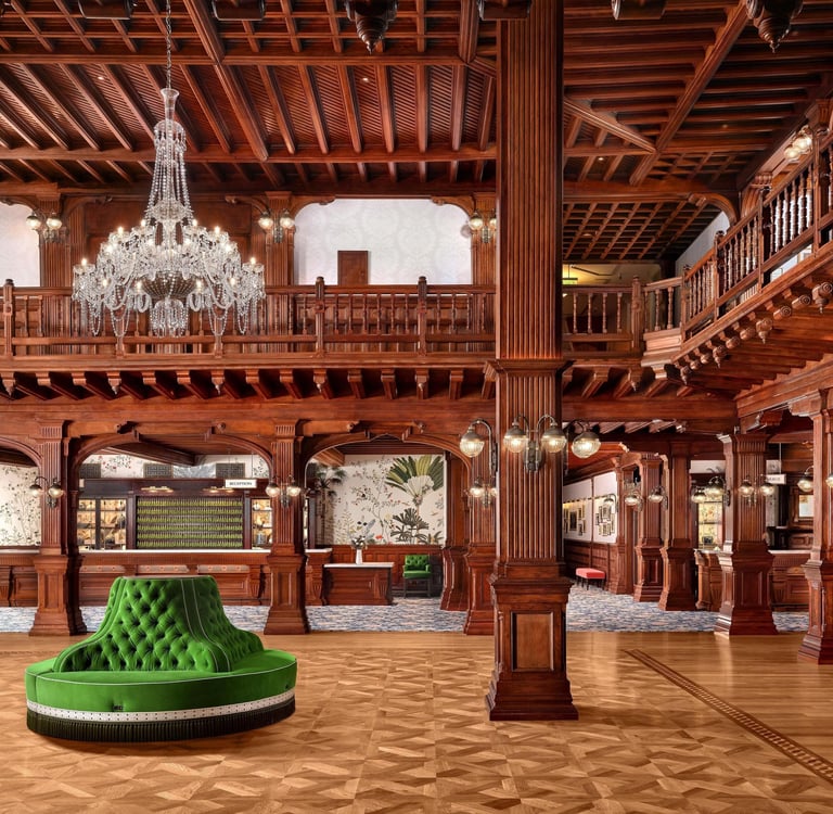 Luxurious hotel lobby featuring ornate wood paneling, a crystal chandelier, and a green velvet circular sofa.