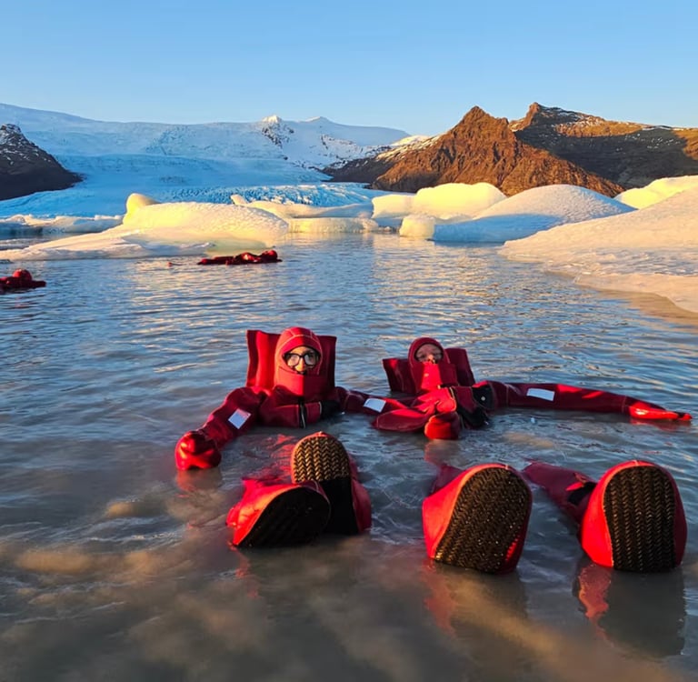 Tourists in red dry suits floating in an Icelandic glacier lagoon surrounded by icebergs.