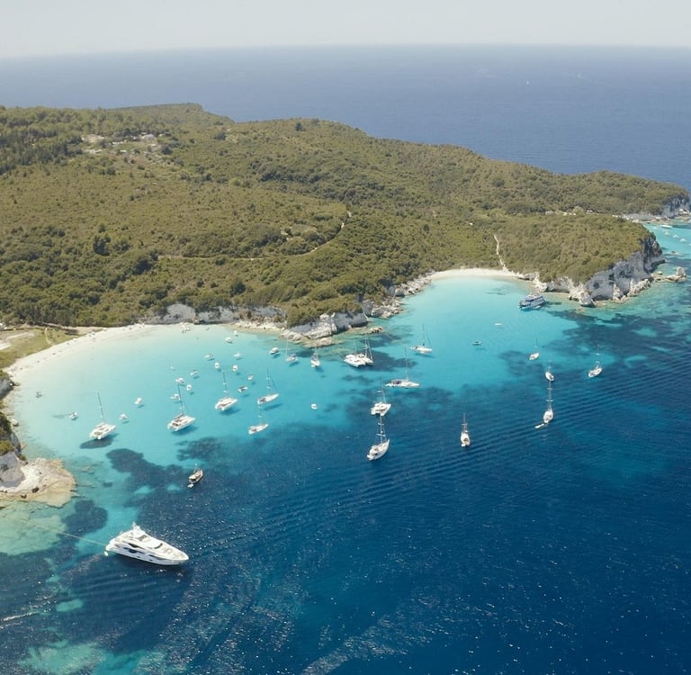 Aerial view of white yachts and sailboats anchored in the turquoise waters of a tropical island bay.