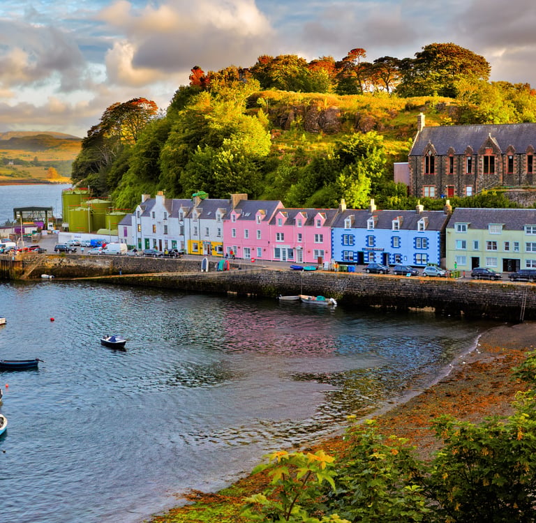 Colorful coastal houses and fishing boats in Portree harbor on the Isle of Skye, Scotland at sunset.
