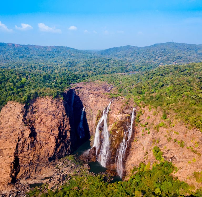 Aerial view of Jog Falls cascading down rocky cliffs surrounded by lush green tropical forests in Karnataka.