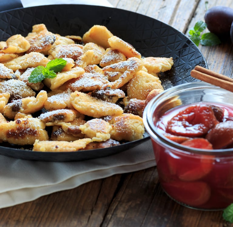 Traditional Austrian Kaiserschmarrn shredded pancake with powdered sugar and plum compote in a jar.