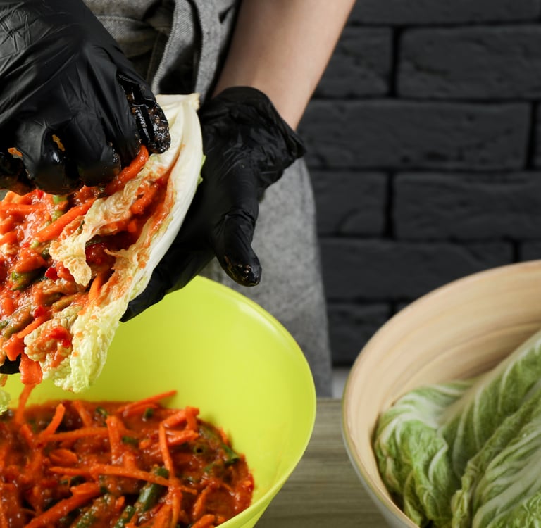 Chef in black gloves preparing authentic spicy Korean kimchi with napa cabbage and red pepper paste.