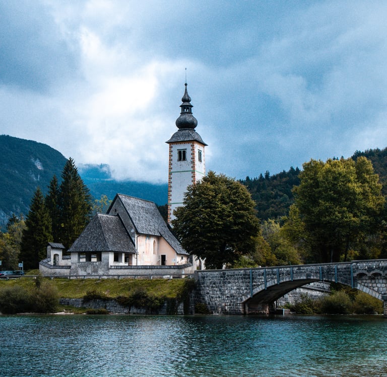 Church of St. John the Baptist and stone bridge on Lake Bohinj, Slovenia, with mountain landscape.