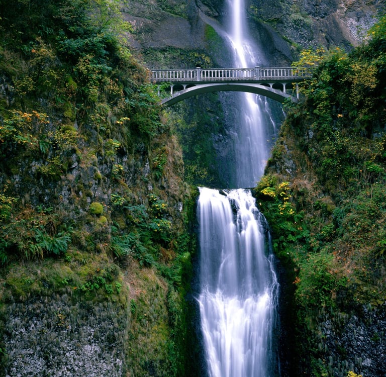 Benson Bridge over Multnomah Falls in the Columbia River Gorge scenic area with lush green cliffs.