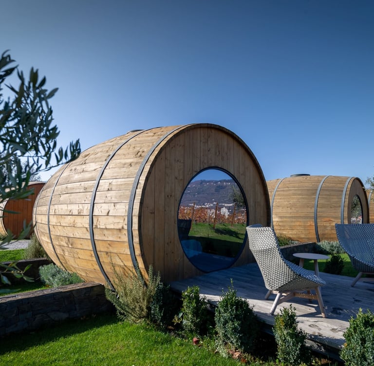 Luxury wine barrel hotel rooms with round windows and private decks overlooking a vineyard resort.