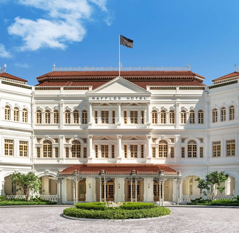 The historic white colonial facade of Raffles Hotel Singapore surrounded by tropical palm trees.