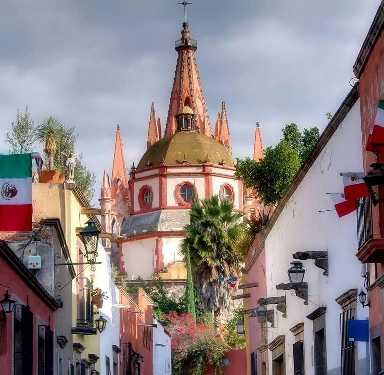 Street view of colonial buildings with Mexican flags and the Parroquia cathedral in San Miguel de Allende.
