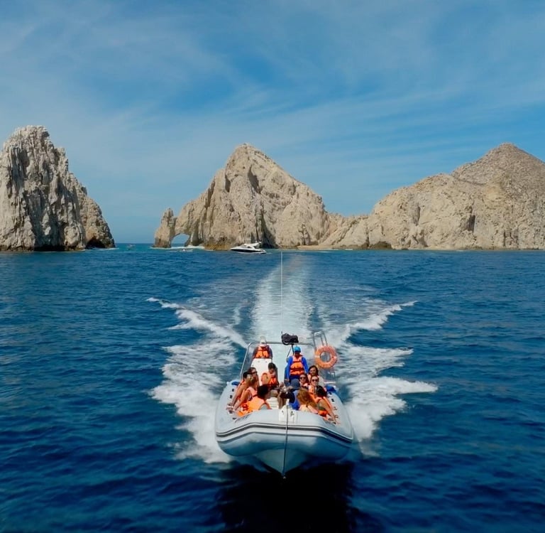 Tourists on a motorboat cruise toward the Arch of Cabo San Lucas in Mexico's blue waters.