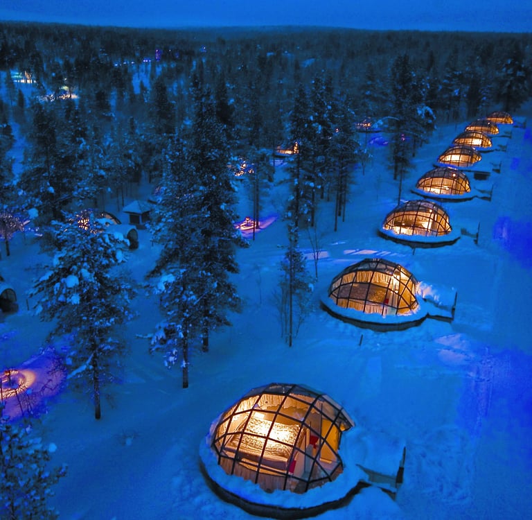 Glowing glass igloos in a snowy Finnish forest at night, perfect for viewing the northern lights.