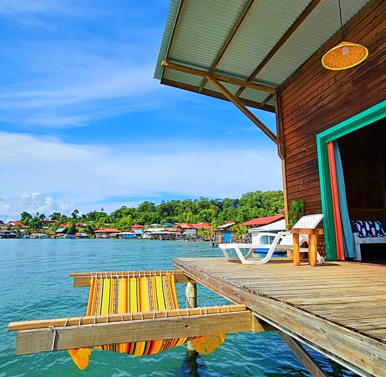 Tropical overwater bungalow with a wooden deck and hammock overlooking turquoise ocean water.