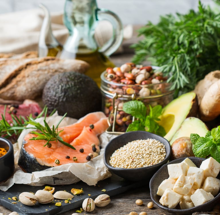 Fresh healthy Mediterranean diet food ingredients including salmon, avocado, vegetables, and nuts on a wooden table.