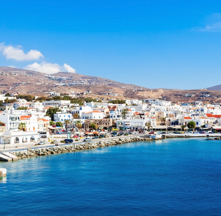 Panoramic view of Tinos town port in Greece featuring white Cycladic houses and blue Aegean Sea.