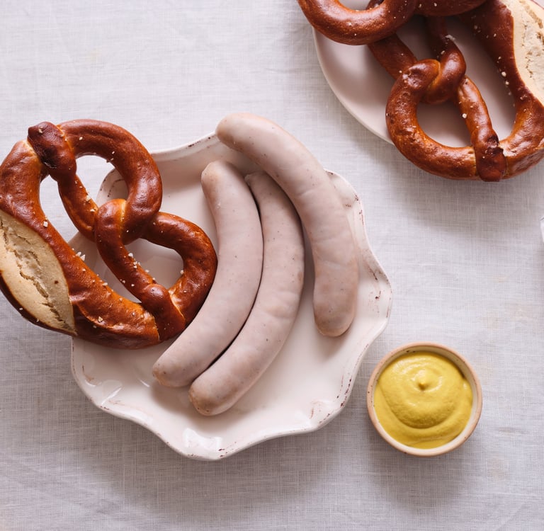 Traditional German breakfast with Weisswurst white sausages, soft pretzels, and sweet mustard on a table.
