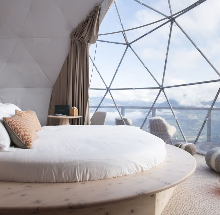 Luxury geodesic dome interior featuring a round bed and scenic mountain views through glass panels.